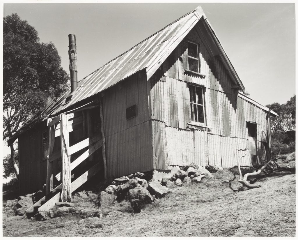 Black and white photograph of a corrugated iron hut with a pitched roof.