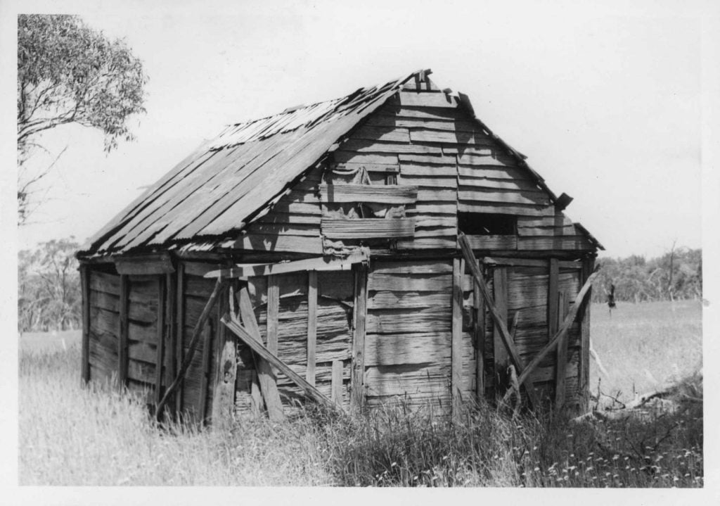 Black and white photograph of a wooden hut in disrepair.