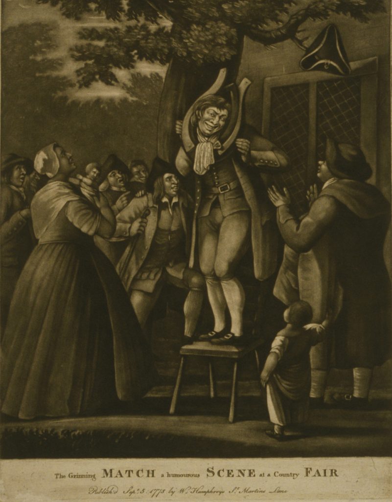 A man stands on a chair beneath a large, spreading tree on which a tri-corn hat hangs from a limb, his grinning face framed by a horse-collar, a woman and a man look on in the foreground, the man applauds, while a crowd of countrymen on the left, in the rear, encourage him with laughter and applause