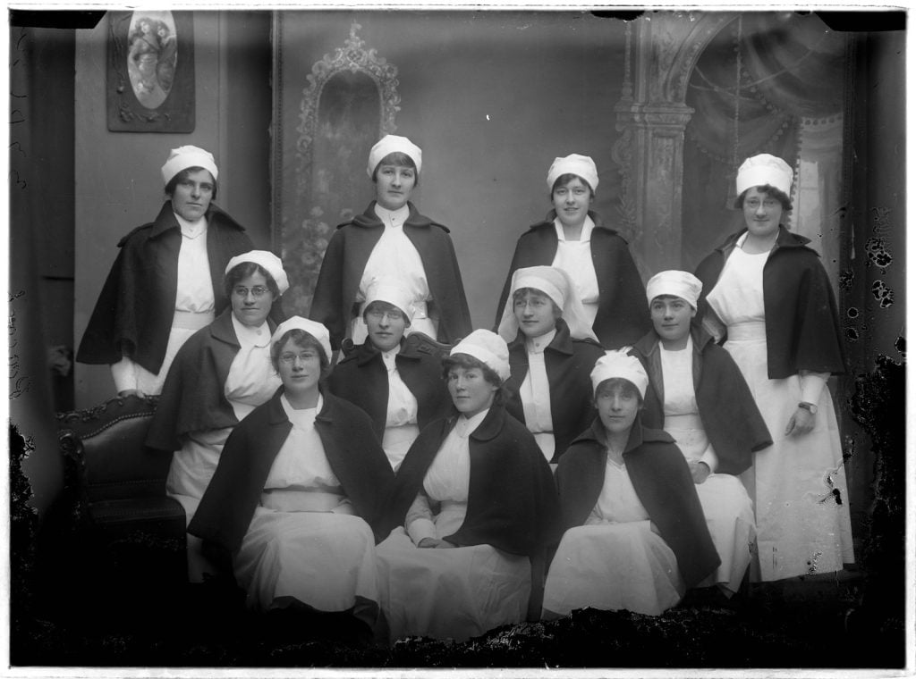 Photographic group portrait of 11 nurses wearing their red caps.