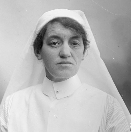 Photographic portrait of Nurse Batterham, wearing white head covering , collar and bib over a pale striped shirt.