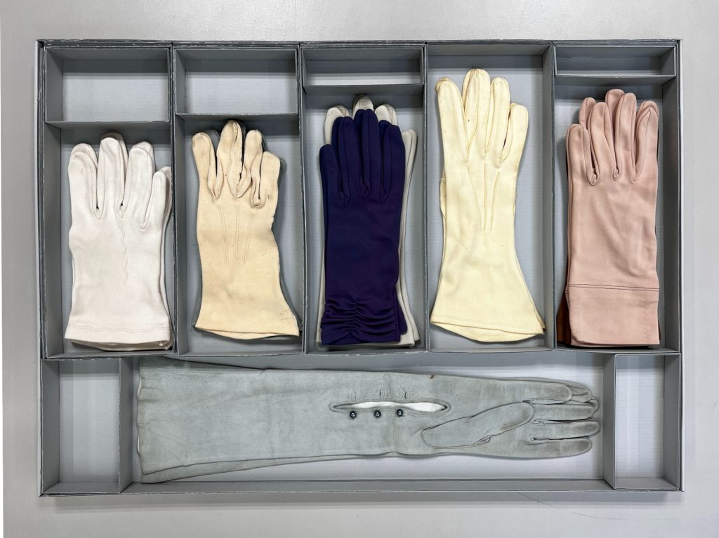 Pastel-coloured vintage ladies' gloves in compartments in a blue-grey archive box