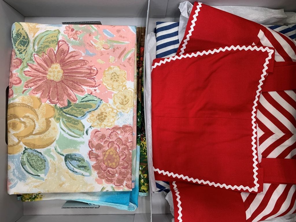 Folded vintage textiles in a blue-grey board archive box. On the left is a textile with a pastel floral pattern. On the right is a bright red and white textile.