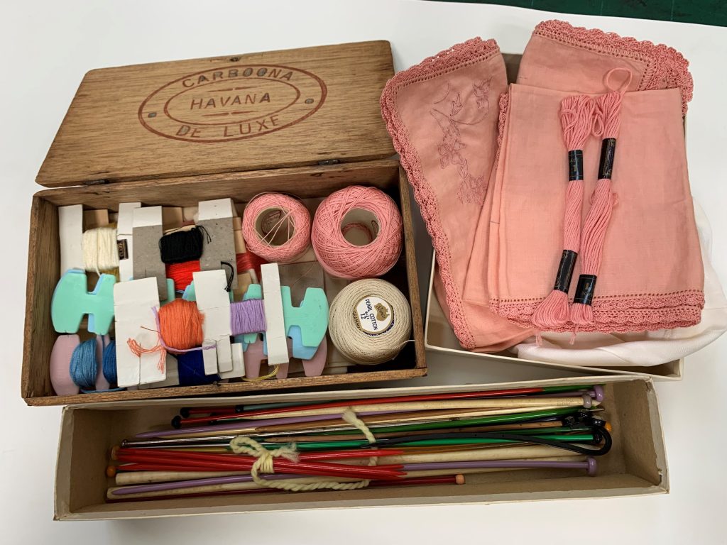 Three boxes on a tabletop containing old sewing threads, linen napkins and knitting needles in many colours