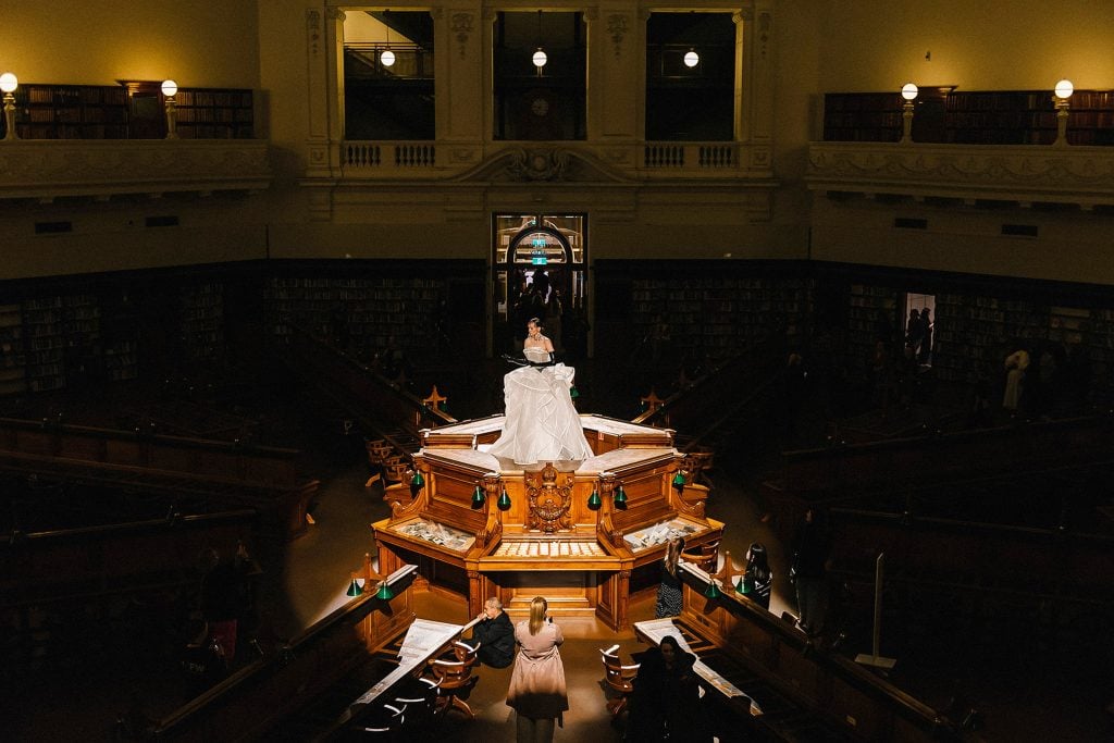 Elevated photograph showing a model wearing a white dress and black gloves, positioned and spotlit on top of the Dais in the centre of the Dome.