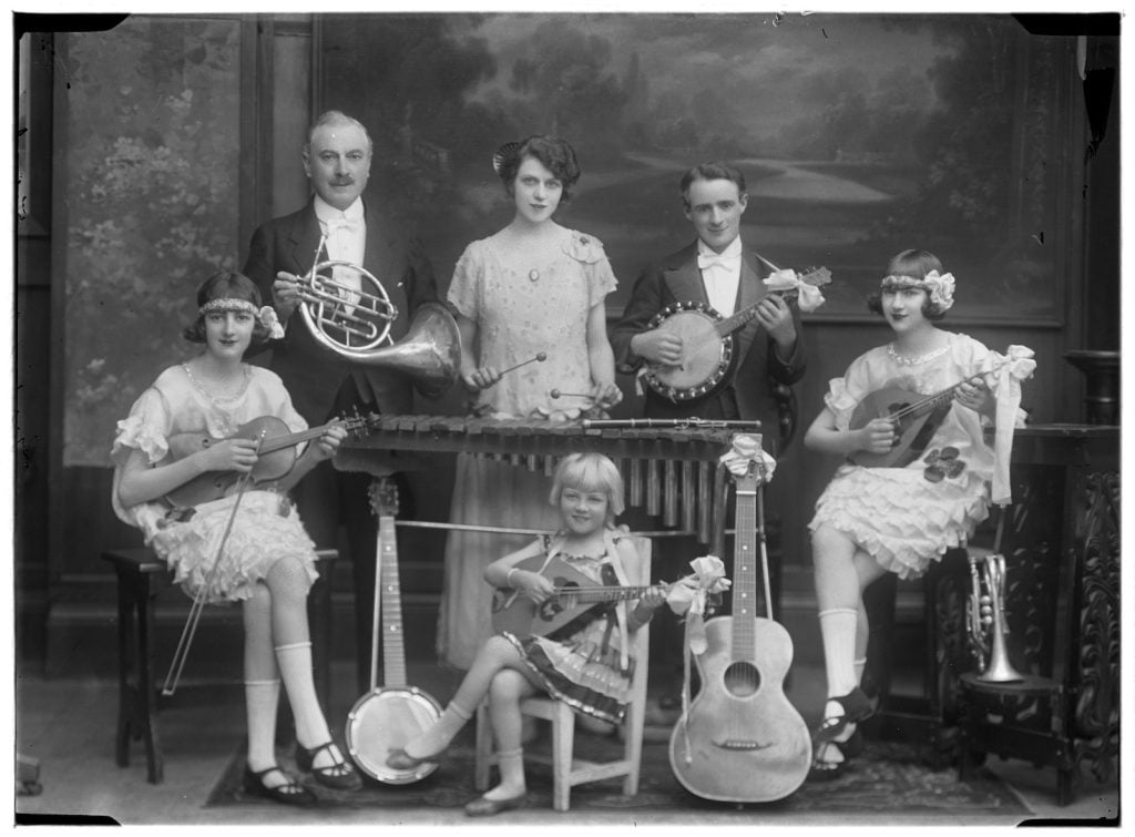 photographic portrait of  6 people 3 adults and 3 children holding musical instruments
