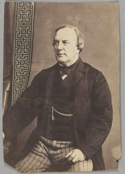 Almost three-quarter length portrait of Augustus Tulk, sitting, wearing striped trousers, jacket and vest, with gold watch chain.