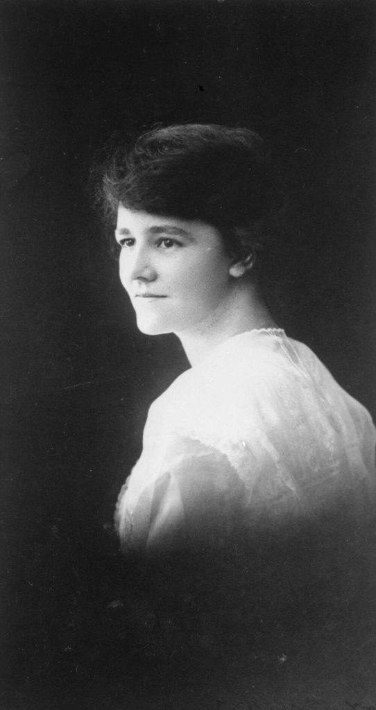 Black and white side portrait of Flora Eldershaw as a young woman. She has short, dark hair and is wearing a white shirt. 