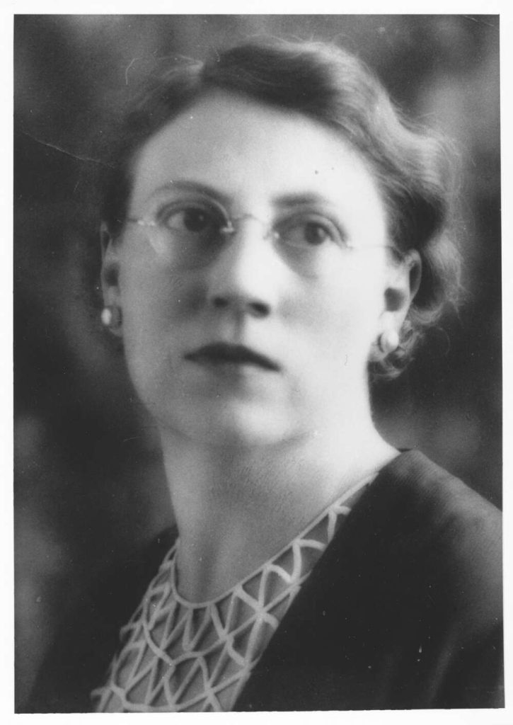 Black and white portrait photo of Marjorie Barnard. She is wearing pearl earrings and round glasses and looking off to the right side of the camera. 