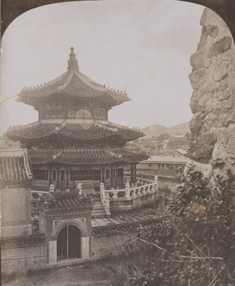 Temple of the Sun, Seoul, Korea, 1905.  The temple is three storeys high with curved roofs and steps at the front. The landscape is rocky. 