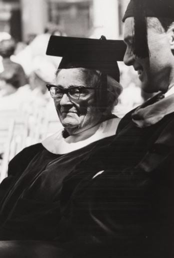 Black and white photographic portrait of a woman wearing a graduation gown and cap.