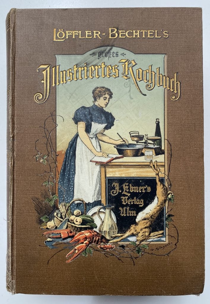 Cover of German cookbook, a woman wearing a blue dress and long white apron, reading a recipe book while stirring, with vegetables, a crayfish and hare arranged on the floor at her feet.