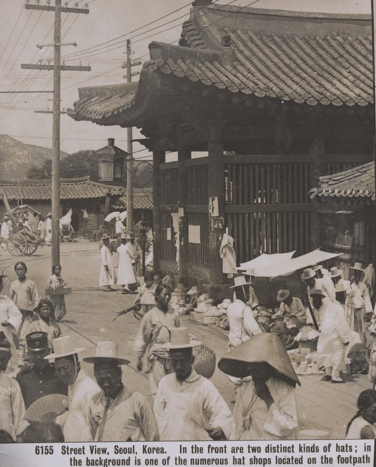 Korean people wearing white clothing and hats walking a busy street. 