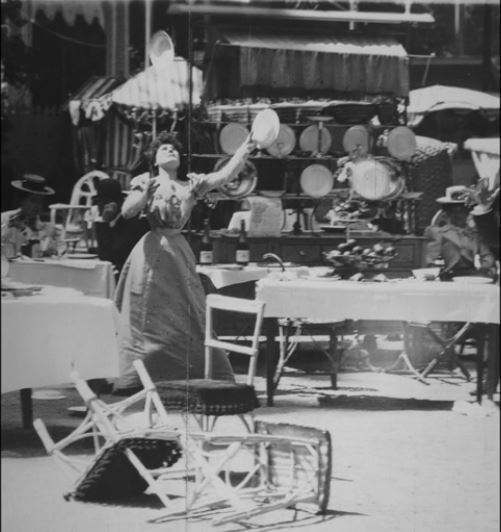 still frame of woman juggling plates. Black and white image.