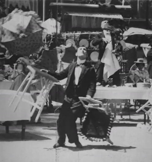 still frame of man juggling two chairs. Black and white image.