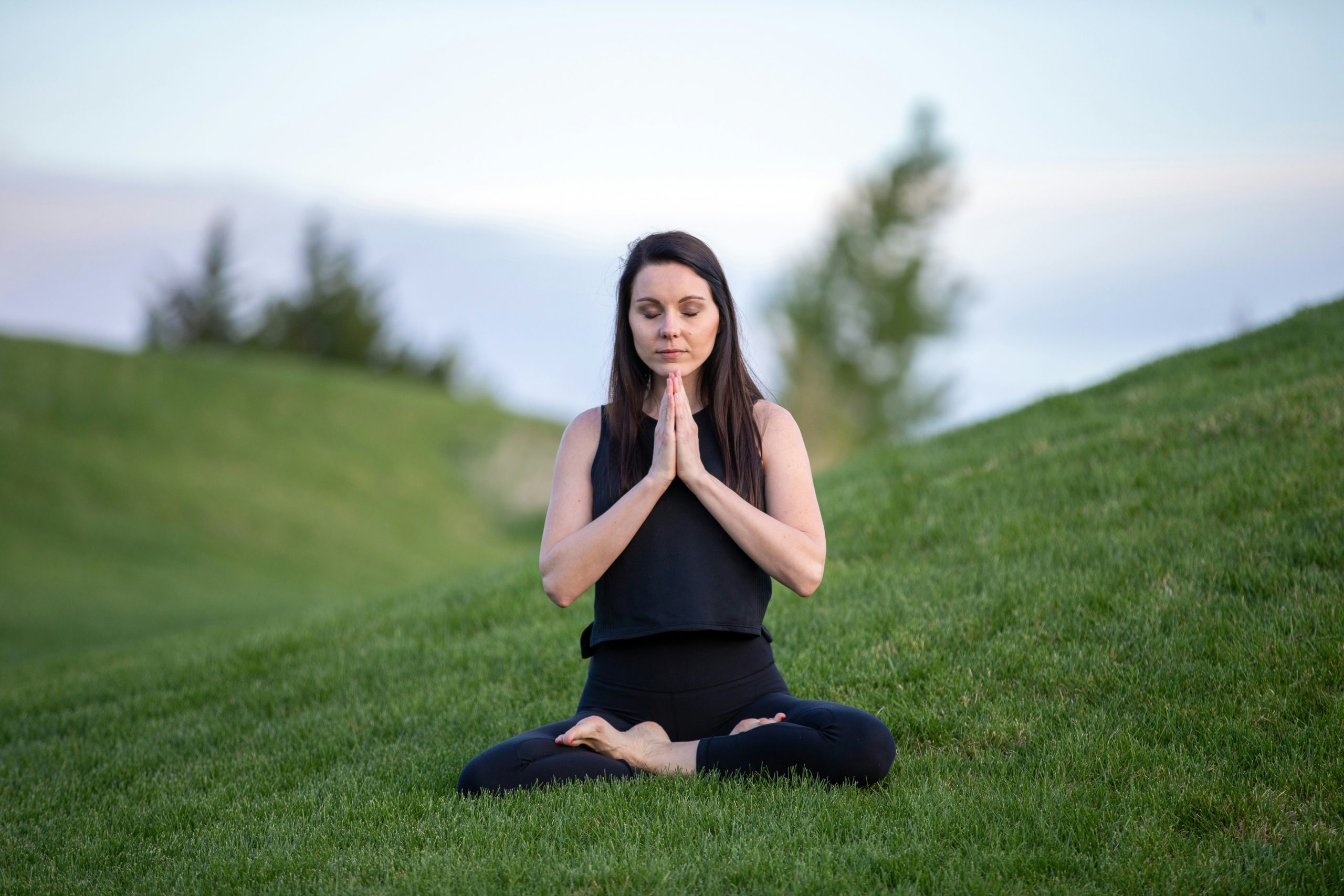 Woman meditating, sitting in yoga pose on green lawn.