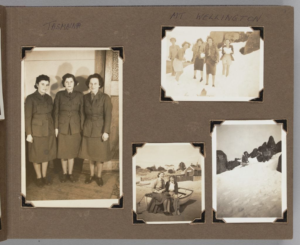 Album page with 4 black and white photographs: 3 women in uniform, a group of 5 women standing in the snow; 2 women sitting on a boat. one woman perched near a rock, snow on the ground.