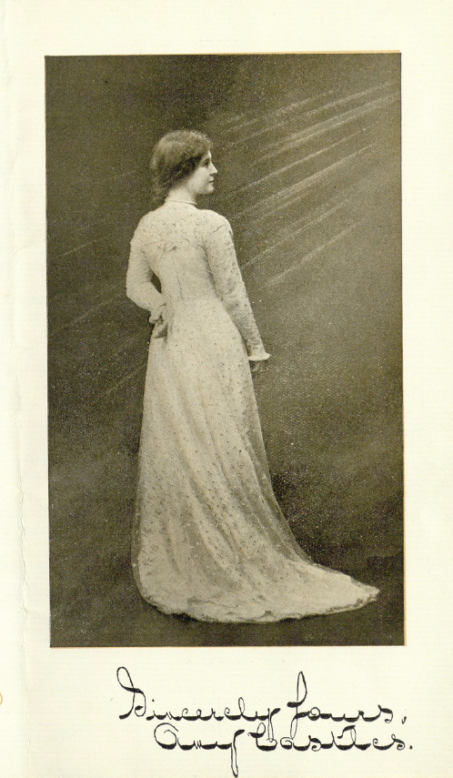 A full portrait of singer Amy Castles in profile with one hand resting on her hip.  She is wearing a full length white gown and a ray of light seems to shine from the right side of the image. The bottom of the image reads 'Sincerely Yours, Amy Castles'.