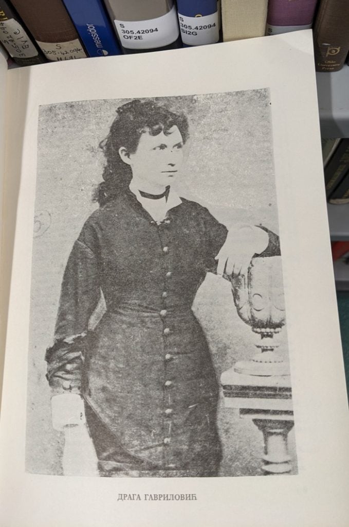 Photograph of a page within a book, showing a photograph of Draga Gavrilovic, a woman wearing a black dress. 