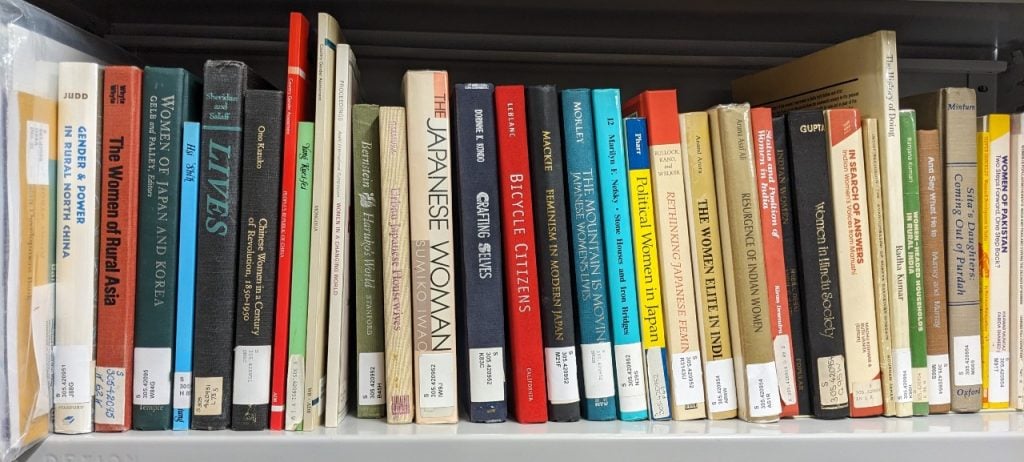 Photograph of a section of books arranged vertically along a metal bookshelf, all with titles relating to "Women in Asia".