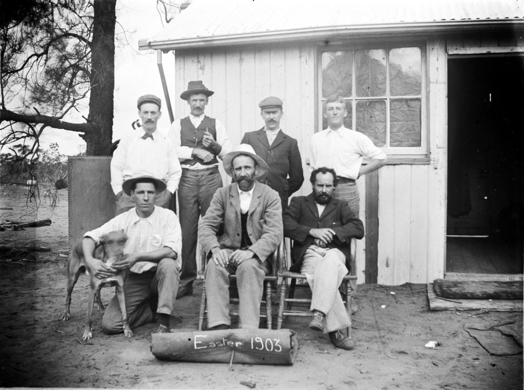 black and white photo of 7 men, railway workers,  - 4 standing 3 seated and a dog, with easter 1903 written on a sign at the front.