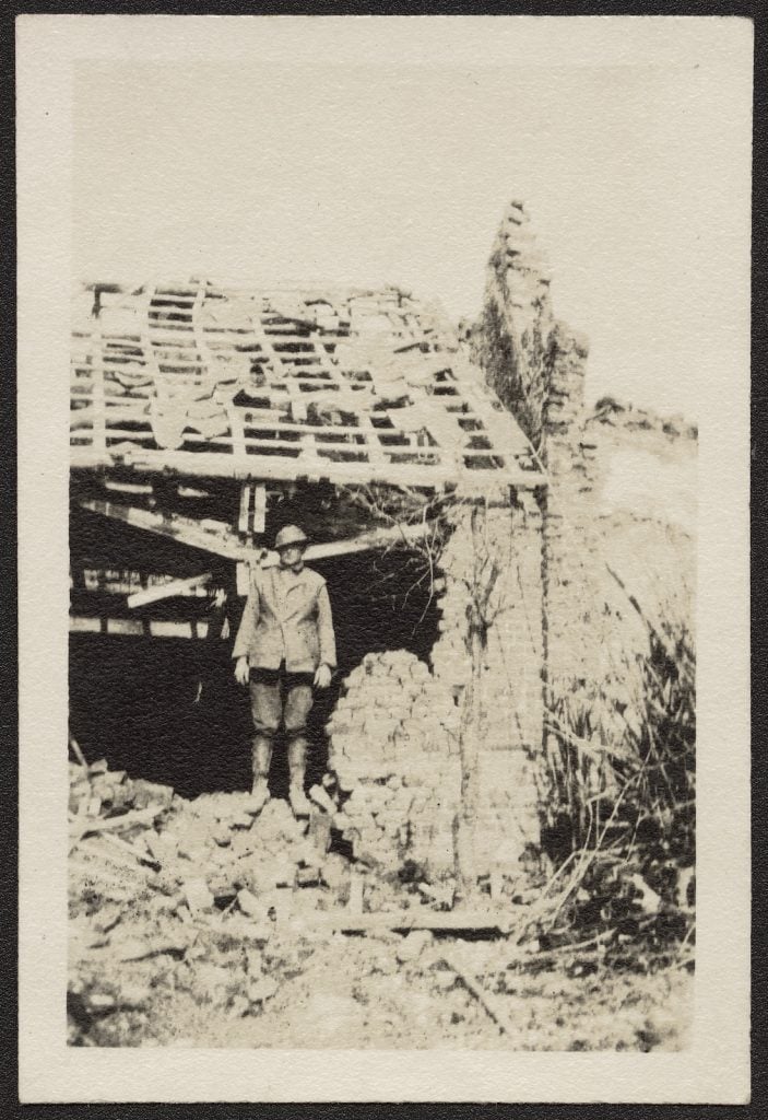 black and white photograph of  a soldier standing under a bombed roof with rubble around
