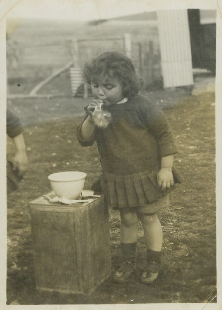 Black and white photograph of a young girl in a dark coloured dress with a pleated shirt, blowing bubbles