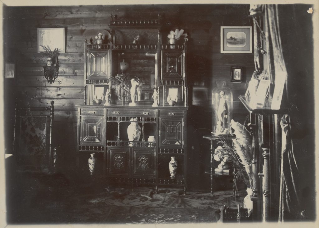 black and white photograph of a richly decorated interior, dark timber walls, a dresser with vases and ornaments, pictures on the wall