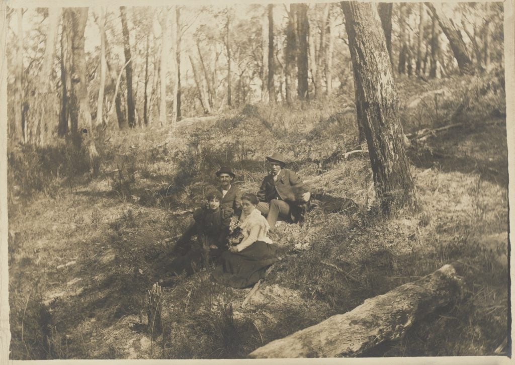 black and white photograph of 4 people on a wooded hillside; photograph of a woman in black standing on a sandy hill in the far distance