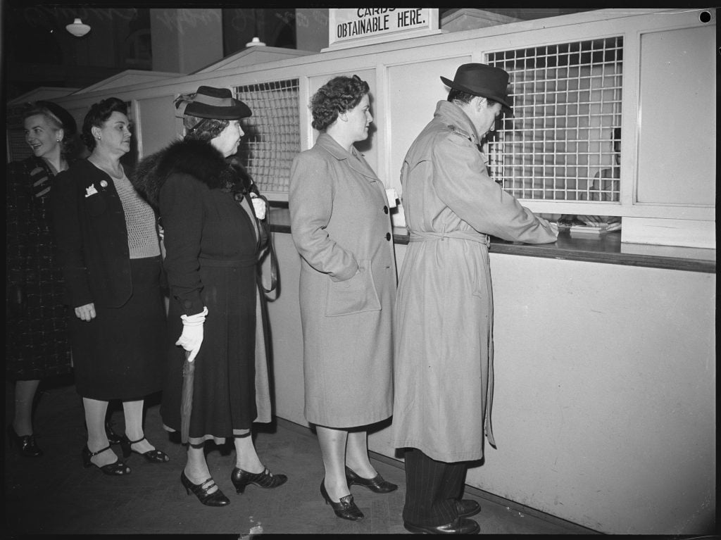 Black and white photo of members of the public lining up to collect their census cards from office window 