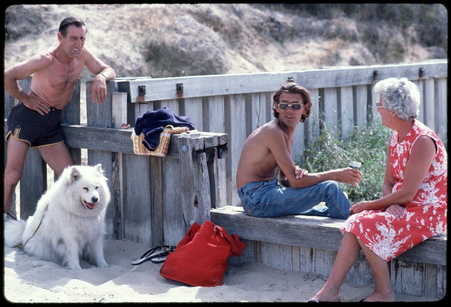 Photograph of two men, a woman and a white husky dog at the beach.