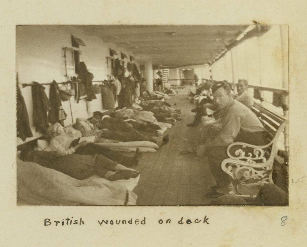 Wounded males on deck of ship. Lying at left and seated at right.