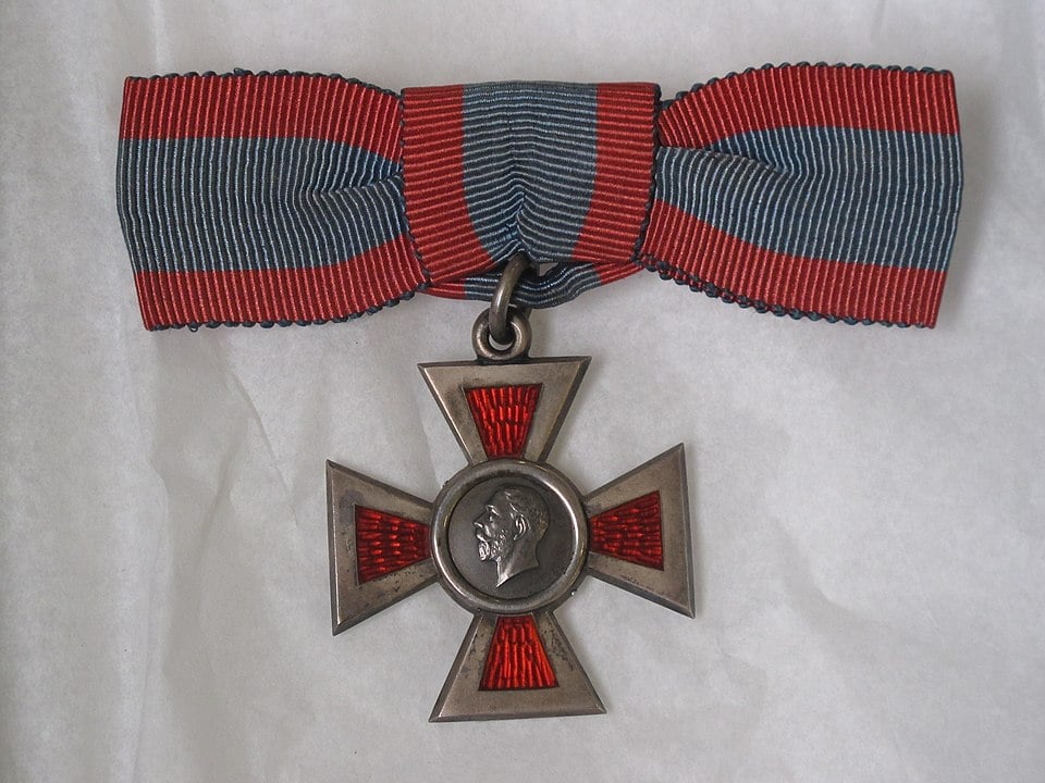 Royal Red Cross 2nd Class WW1 silver cross with red inlay, 35 mm width, plain ring suspension on a red and blue cloth ribbon. White background.