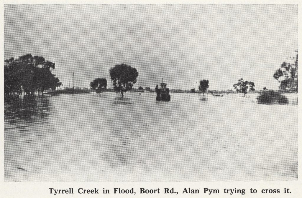 Black and white photo of Tyrell Creek, flooded. A farmer is trying to cross it on a tractor in the distance. 