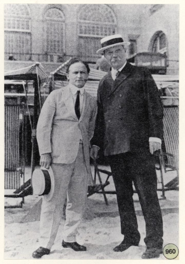 Harry Houdini in white suit standing with Arthur Conan Doyle in dark suit with boater hat