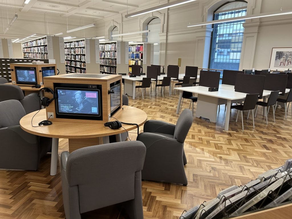 Room with tables, chairs, bookshelves, TV screens and headphones