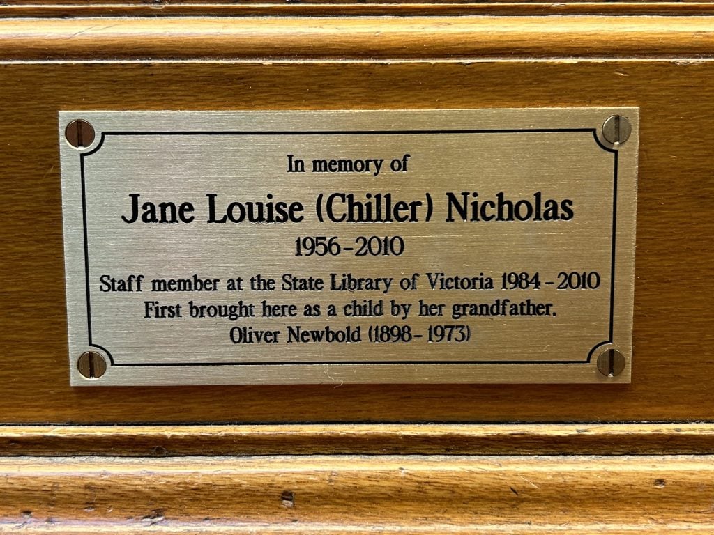 Gold plaque that reads In memory of Jane Louise (Chiller) Nicholas  1956-2010. Staff member at the State Library of Victoria 1984-2010. First brought here as a child by her grandfather, Oliver Newbold (1898-1973)