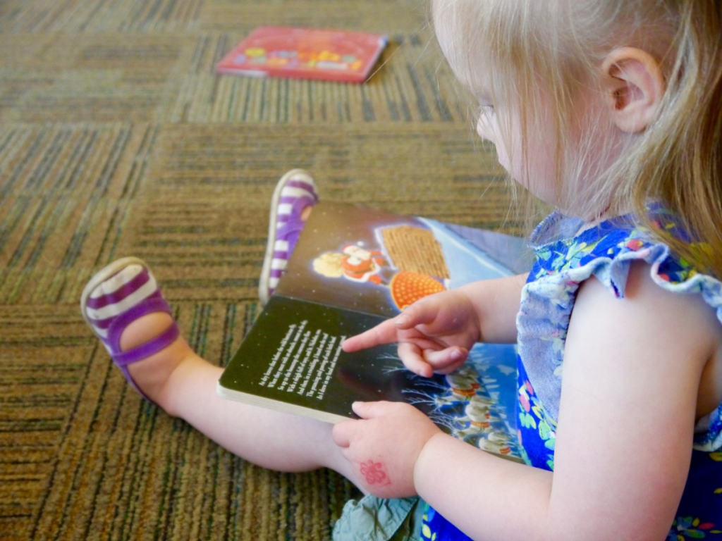 Colour photograph of a toddler sitting on the floor and reading a book