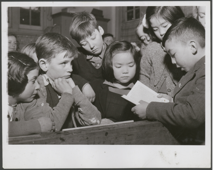 Black and white photograph shows Chinese boy reading a book, surrounded by other children.