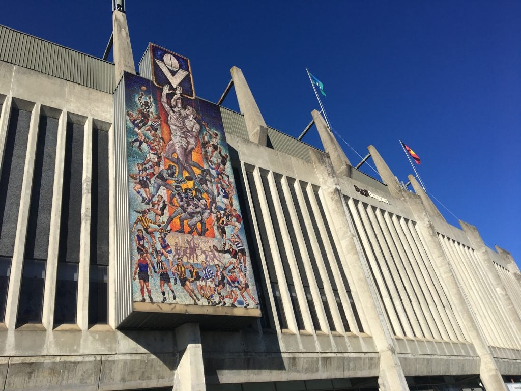 The Greats of Football mural placed against a large concrete grandstand with thin vertical partitions. 