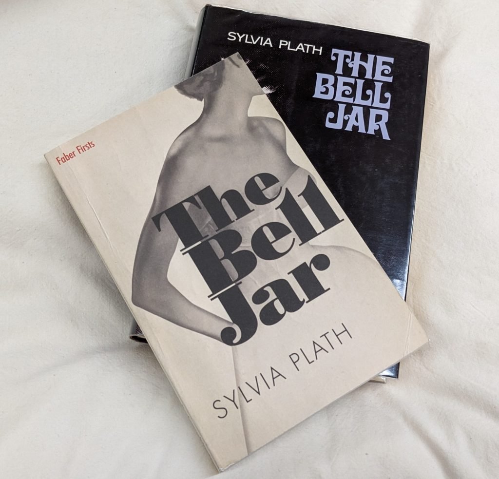 Photograph of two versions of The Bell Jar by Sylvia Plath, sitting on top of each other, slightly fanned out, on top of a pillow. 