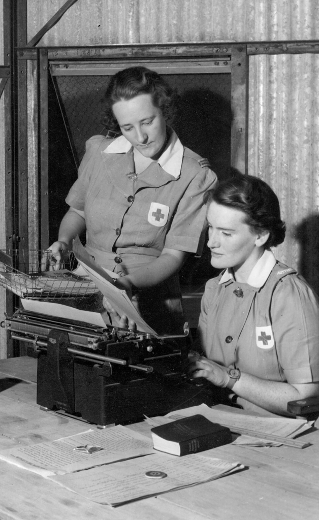 Shows Nancy Hutchinson and Betty Davidson, one woman typing the other holding a tray of papers.