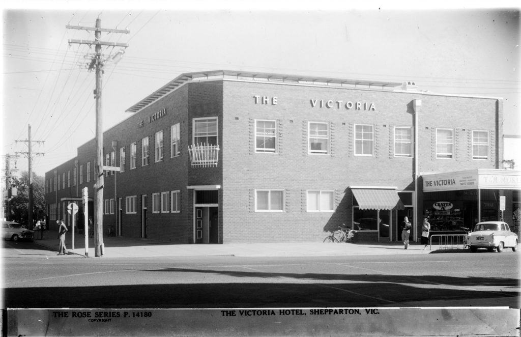 black and white photograph of the Victoria Hotel located on a street corner. There is an old car parked out the front and a man standing on the footpath.