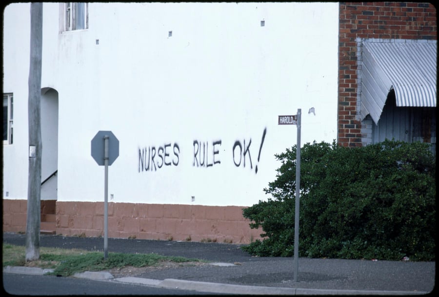 Graffiti on the side of a house saying 'nurses rule ok!'