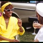 Woman dressed in yellow talking to a woman dressed in white.