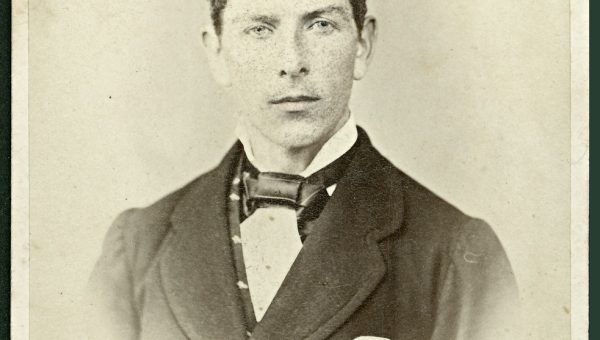 black and white photograph of young man wearing suit and necktie. Dark hair parted in the middle and slicked down.