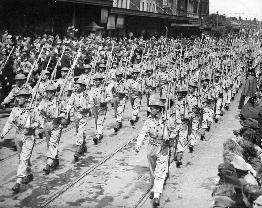 Shows Royal Australian Air Force troops parading down a city street, with crowds cheering them on.