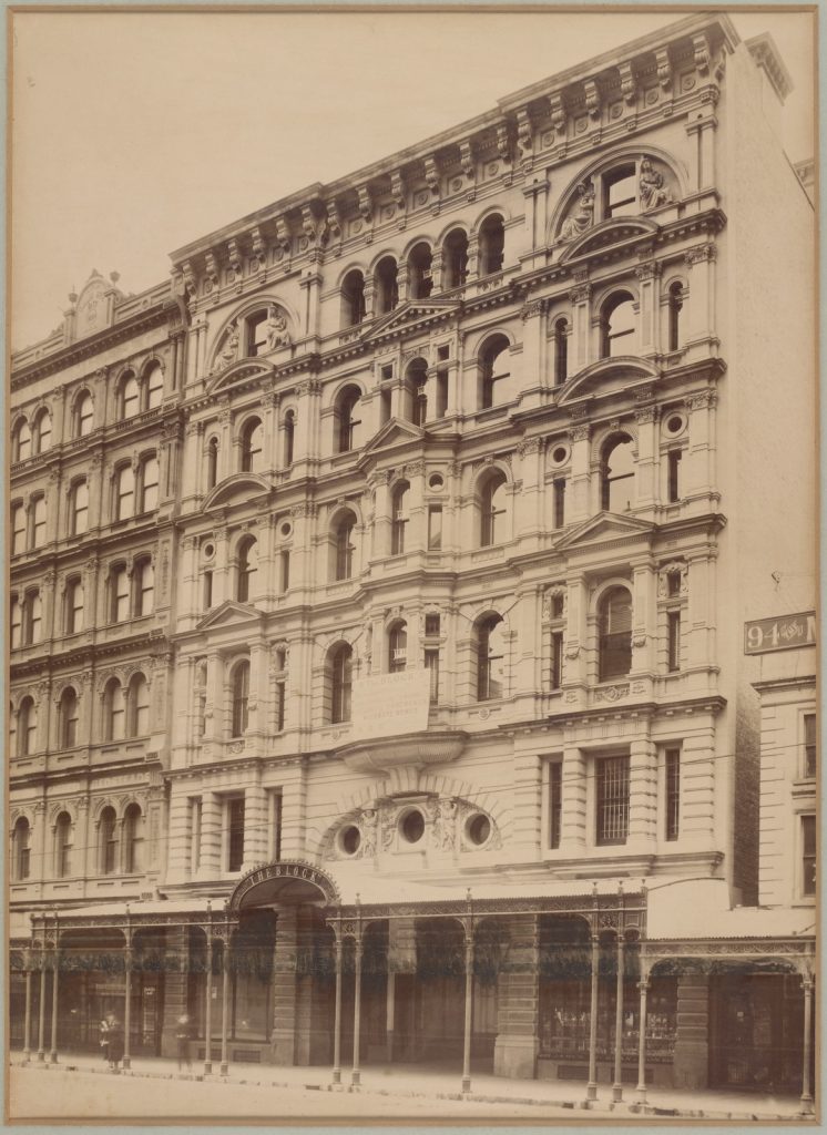Photograph of the Block Arcade, Melbourne, ca. 1890. Shows six storey building, designed by D. C. Askew, with verandah and wrought iron lace work at street level. Two people stand on footpath l.l.