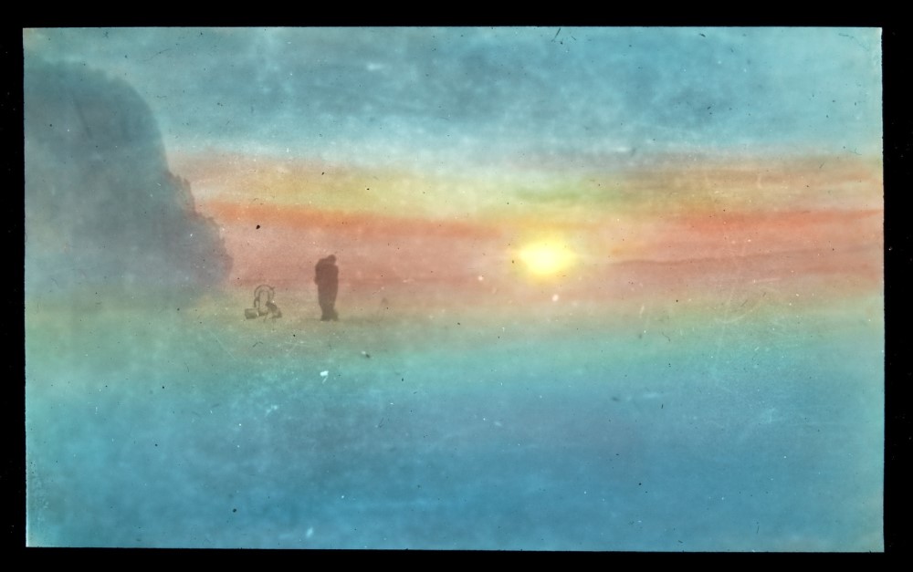 Sun low across Antarctic landscape with man and sled