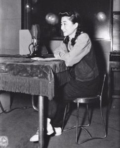 Re-enactment. Iva Toguri sits at desk with microphone.